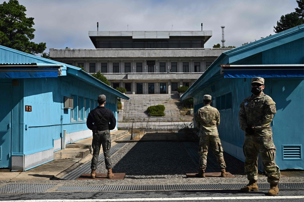 In this file photo taken on October 4, 2022, UNC (United Nations Command) soldiers (right) and a South Korean soldier (left) stand guard before North Korea's Panmon Hall (rear C) and the military demarcation line separating North and South Korea, at Panmunjom, in the Joint Security Area (JSA) of the Demilitarised Zone (DMZ). Twenty-five years ago, a desperate director risked jail to make a movie about an unlikely friendship between North and South Korean soldiers, striking box office gold and launching his actors to global stardom today. — AFP pic