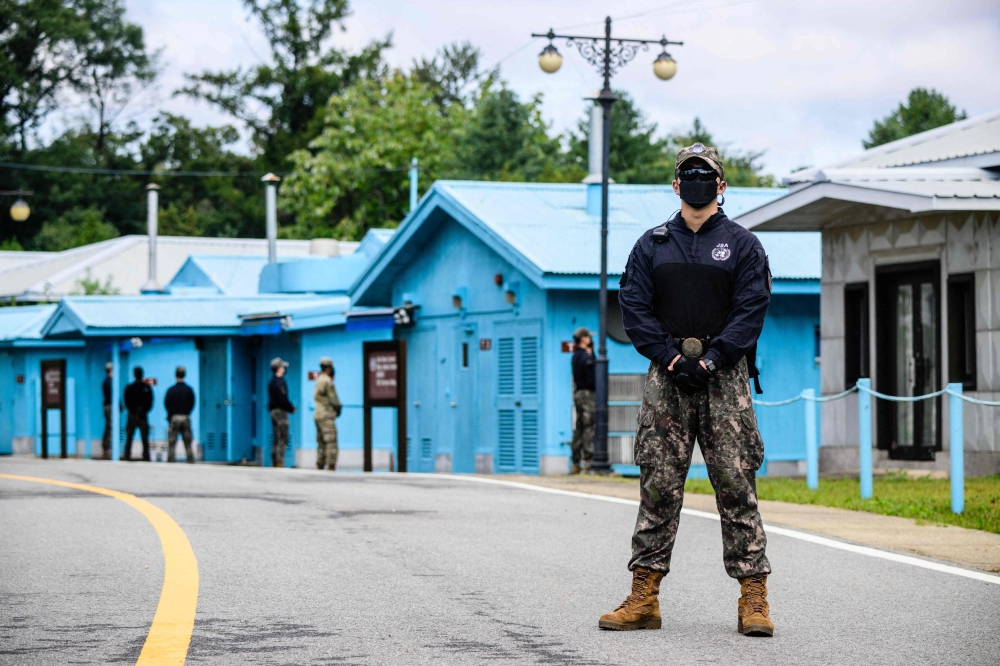 In this file photo taken on October 4, 2022, a South Korean soldier (R) and UNC (United Nations Command) soldiers (background, in green) stand guard near the military demarcation line (not seen) separating North and South Korea, at the Joint Security Area (JSA) of the Demilitarised Zone (DMZ) in the truce village of Panmunjom. — AFP pic