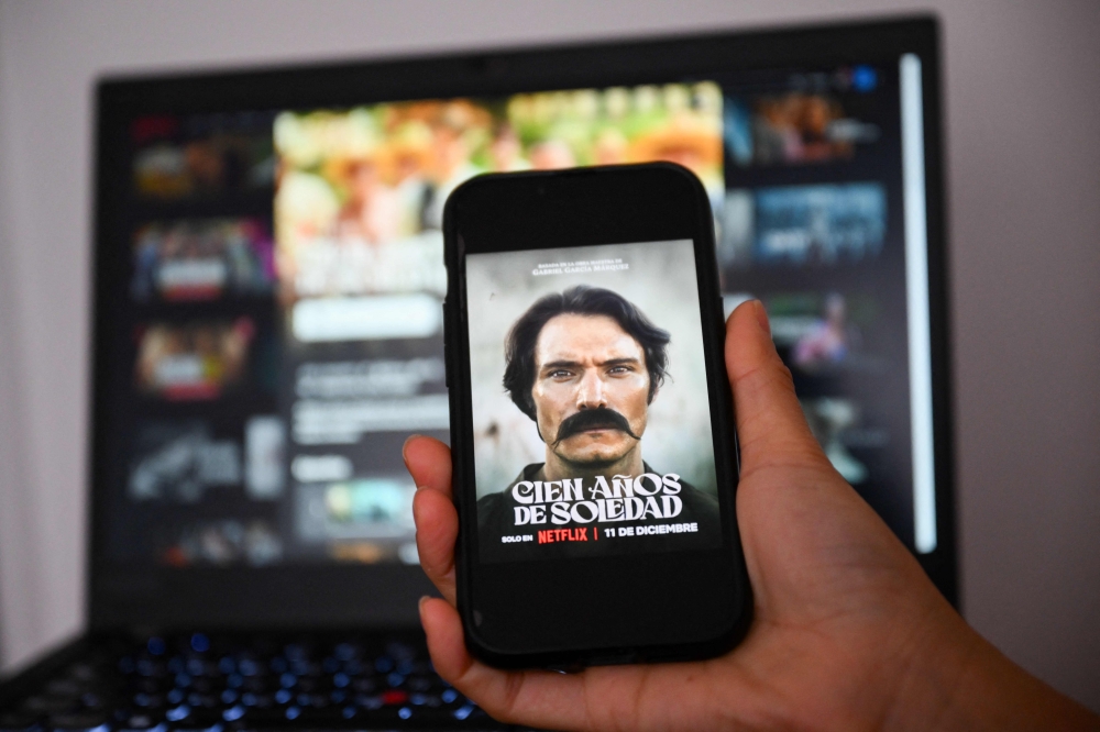 Photo illustration taken on February 5, 2025, in Buenos Aires, Argentina, of a woman holding a mobile phone with the image of the Netflix streaming television series ‘Cien Anos de Soledad’. — AFP pic